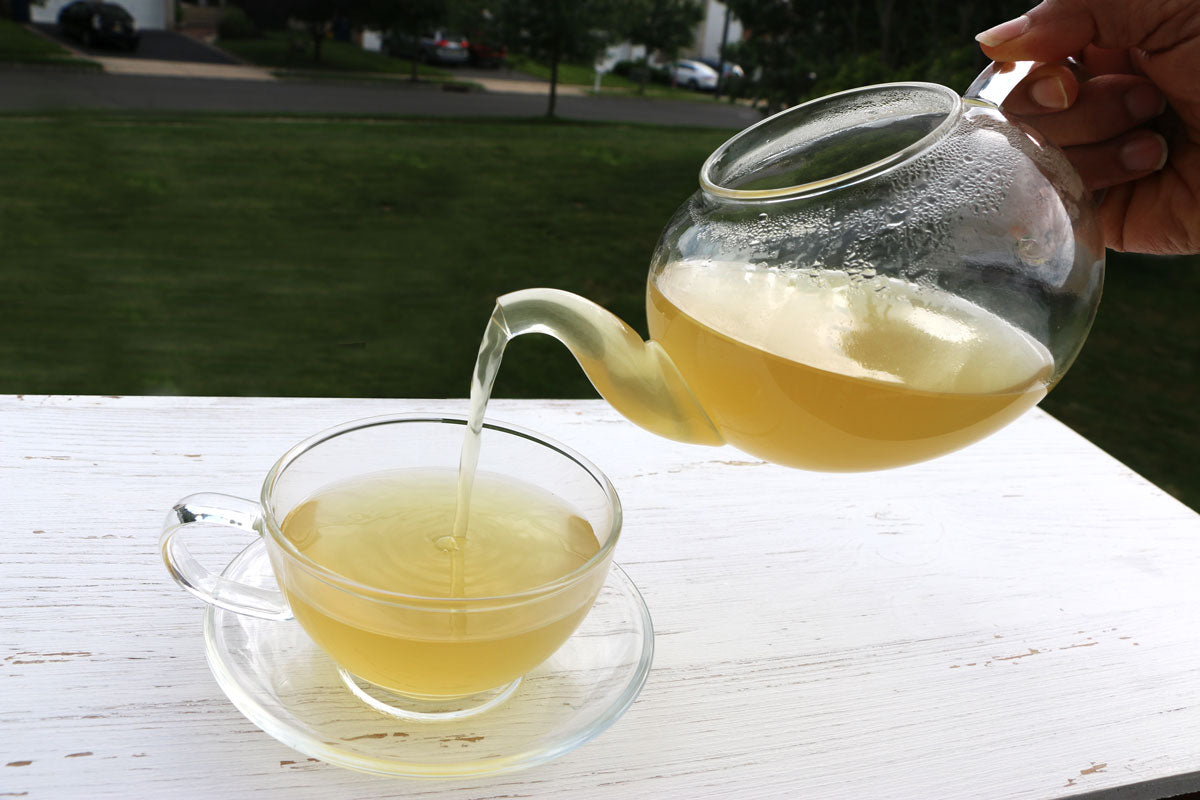 Glass teapot full of freshly brewed CCF Tea pouring a serving into a glass teacup.