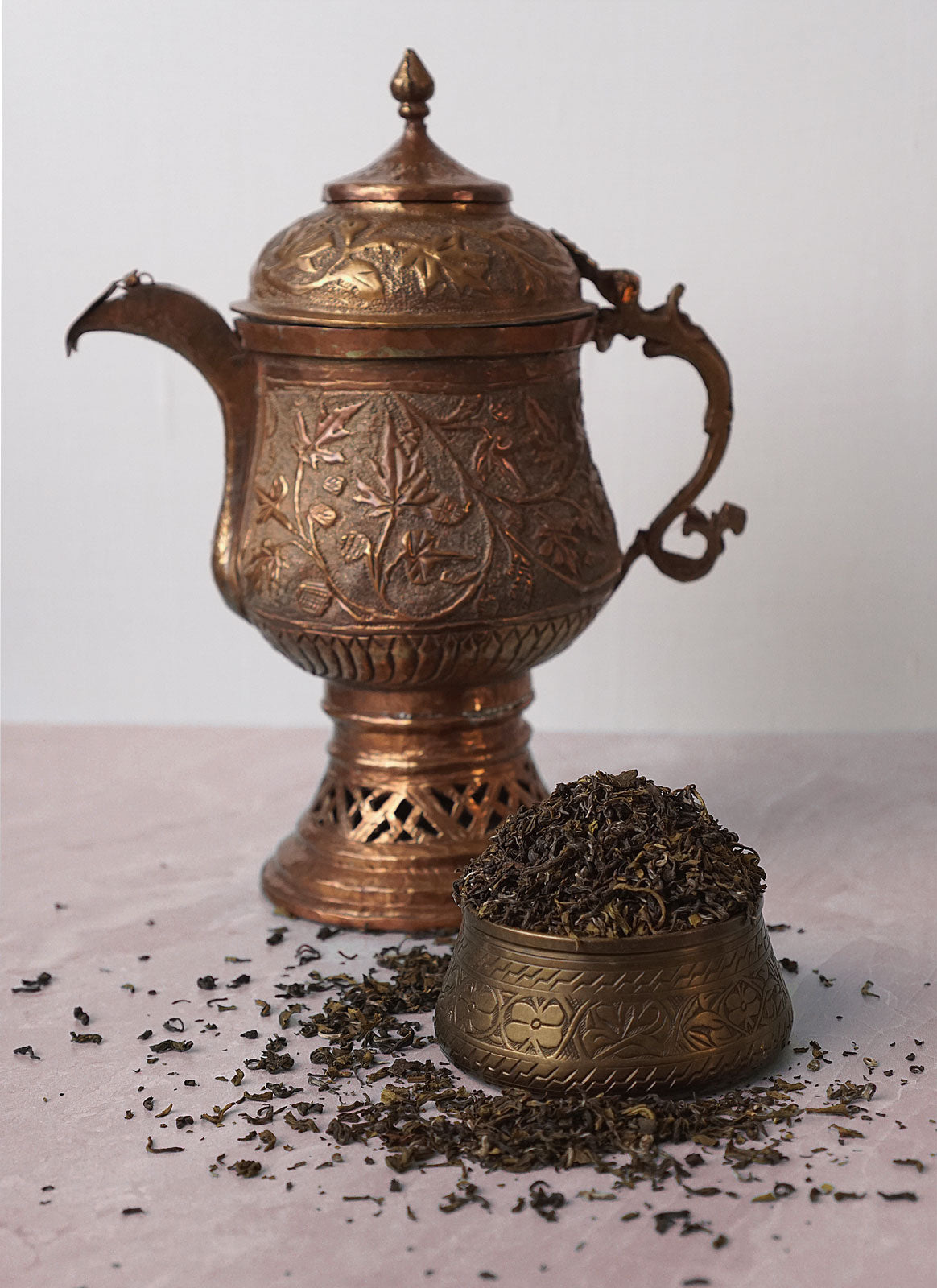 Antique copper tea pot and cup with scattered loose leaf pure darjeeling tea.