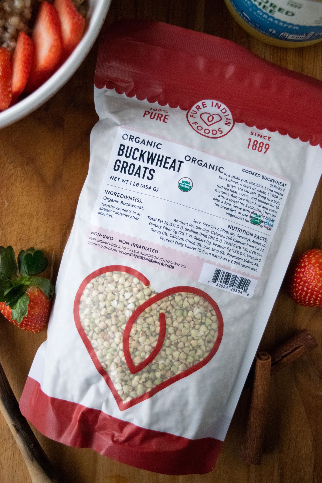 1 bag of organic buckwheat groats, displayed on a wood background next to whole cinnamon sticks, fresh strawberries, and a jar of our grassfed organic cultured ghee