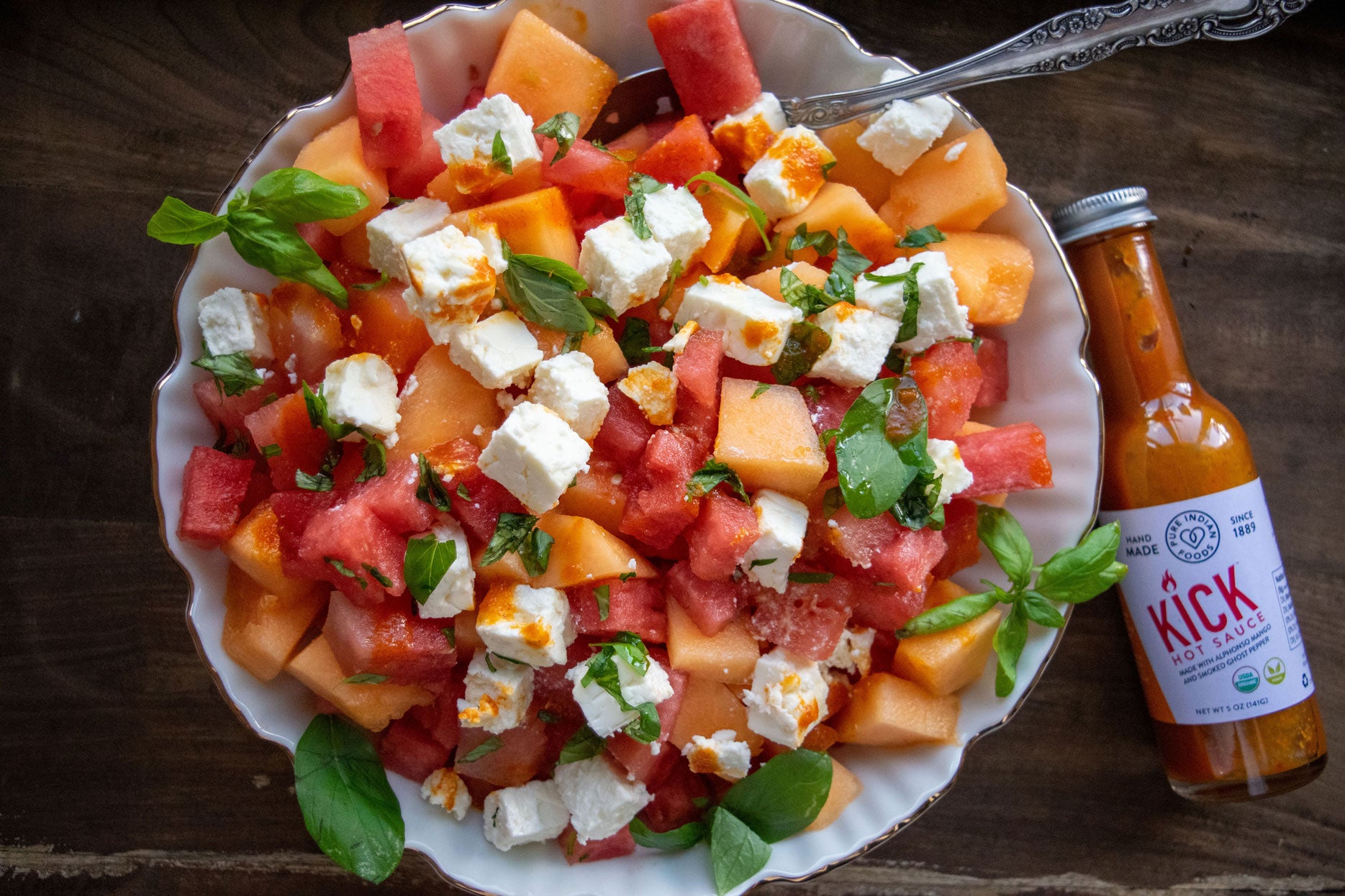 Summer salad of cubed canteloupe, watermelon, cheese, with honey and basil and featuring our Pure Indian Foods KICK Hot Sauce, an organic Mango Ghost pepper hot sauce.