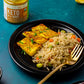 A plate of indian rice pilaf and grilled tempeh made with our keto curry sauce. In the background, there's an open jar of Keto In A Hurry Madras Curry Sauce.