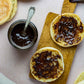 Jar of organic chyavanprash jam from Pure Indian Foods, spread on an open English muffin, displayed on a small wood board.