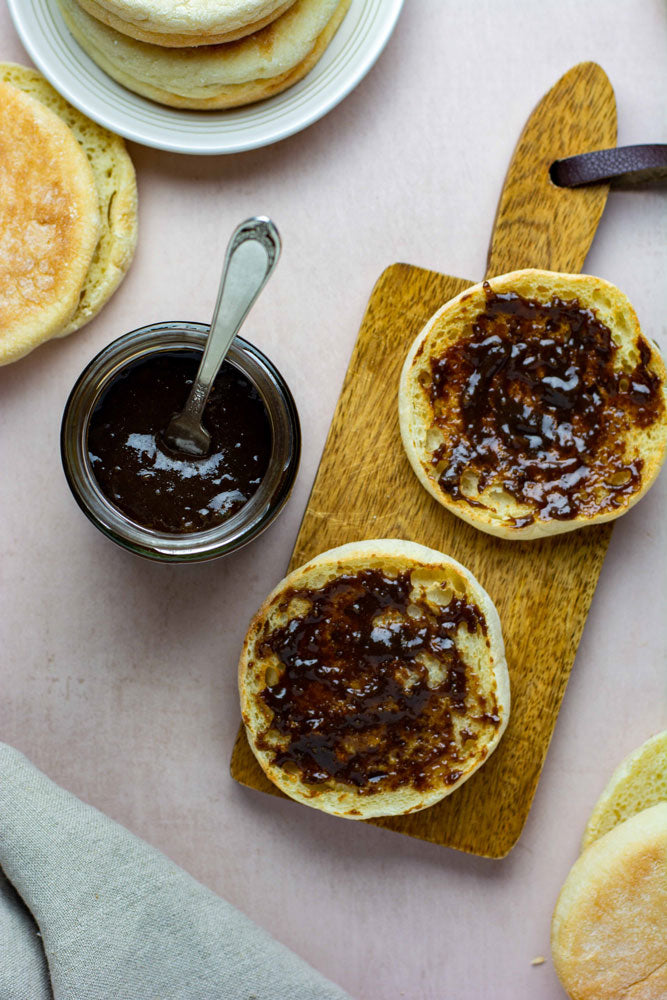 Jar of organic chyavanprash jam from Pure Indian Foods, spread on an open English muffin, displayed on a small wood board.