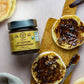 Jar of Pure Indian Foods organic chyawanprash jam, spread on a halved English muffin, displayed on a board with a small butter knife.