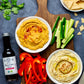Hummus and dips on a serving board with freshly sliced veggies and chips, staged next to a jar of vegan Worcestershire sauce from Pure Indian Foods.