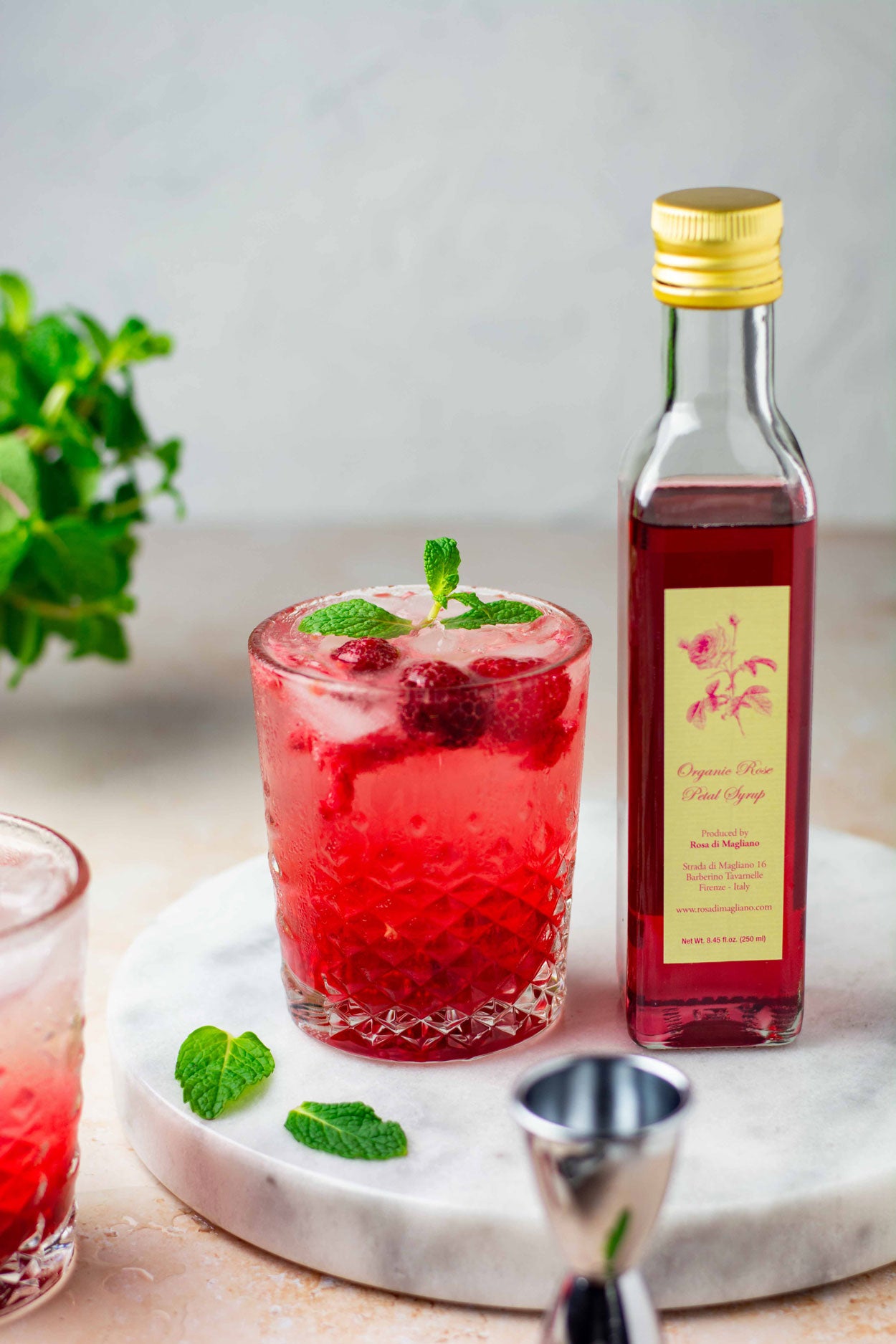 Homemade cocktail in a crystal tumbler using our organic rose simple syrup and fresh mint leaves, resting on a marble slab.