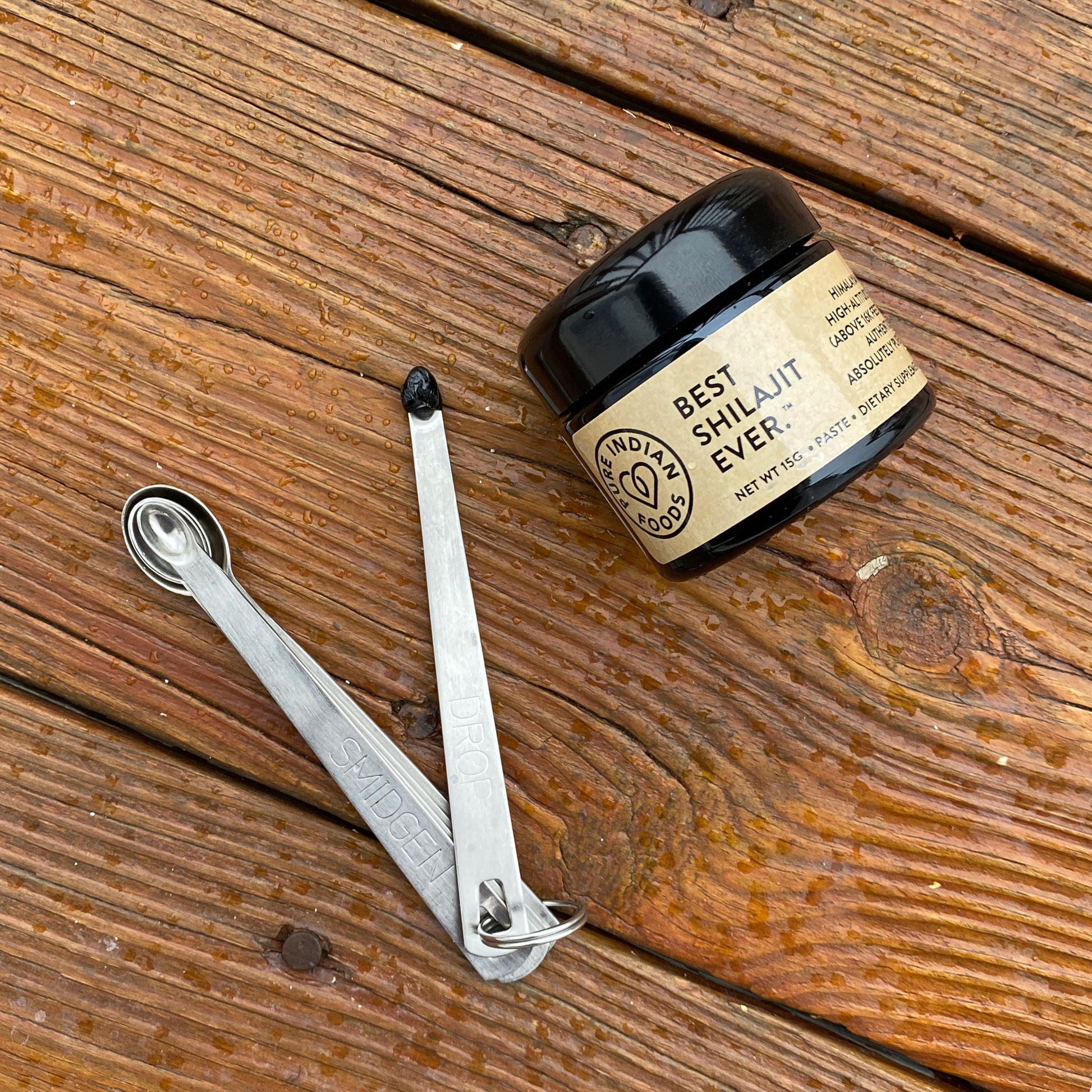 Jar of the Best Shilajit Ever, a high-altitude himalayan shilajit, on a wooden background, next to a tiny spoon with the pure shilajit resin scooped into it. 