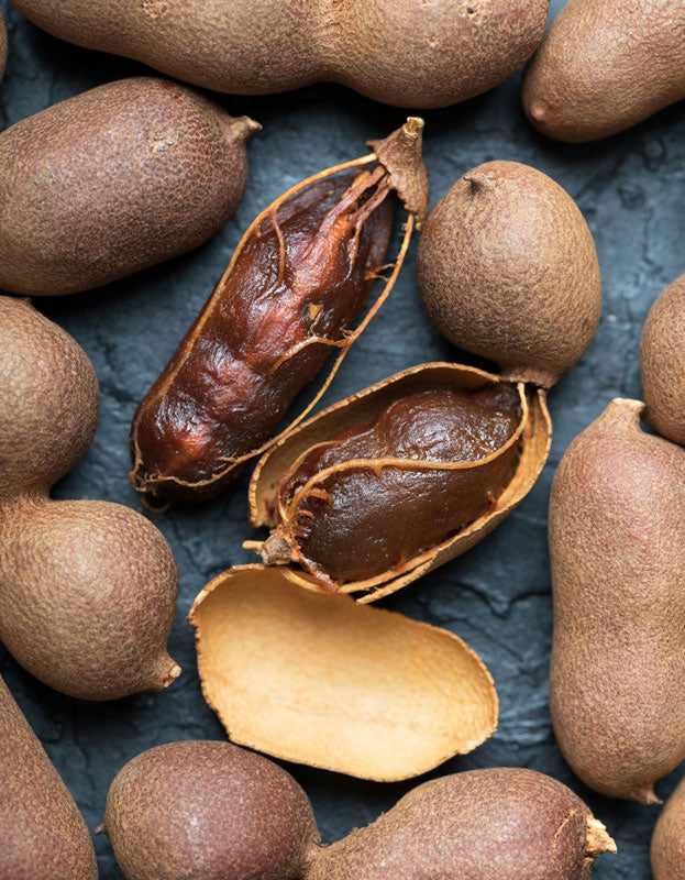 Organic tamarind pods, two of which are broken open to reveal the fruit inside.