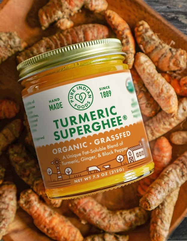 A jar of Pure Indian Foods Turmeric Superghee on a bed of fresh turmeric root.