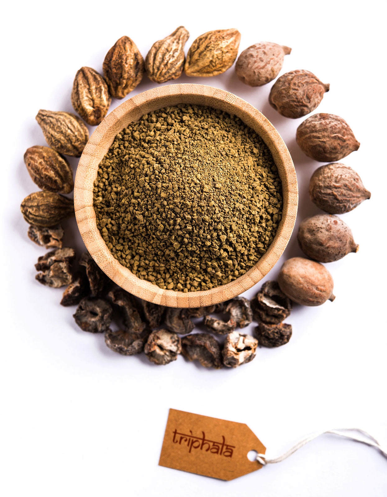 a bowl of triphala powder surrounded by dried Amla, Haritaki, & Bibhitaki fruits