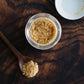 spoonful of asafetida powder on a wooden table near an open jar of hing