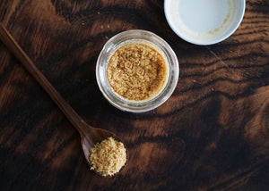 spoonful of asafetida powder on a wooden table near an open jar of hing