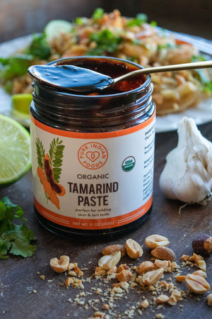 Open jar of organic tamarind Paste from Pure Indian Foods, with a spoon dipped into it. Label says it's perfect for adding sour and tart taste to your food.
